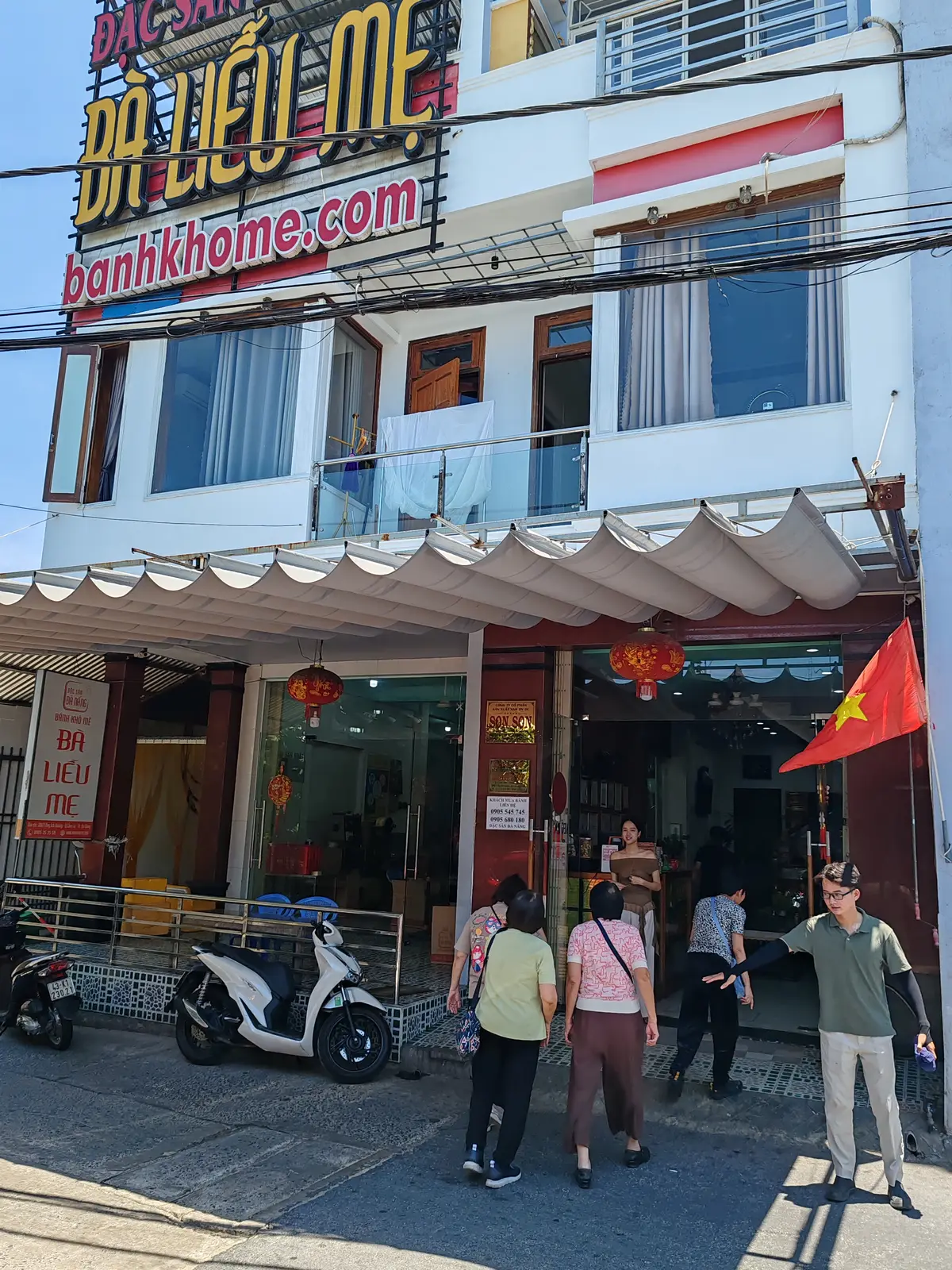Mặt tiền cơ sở bánh khô mè Bà Liễu Mẹ trên đường Ông Ích Đường, có cờ đỏ, đèn lồng và khách ở lối vào.