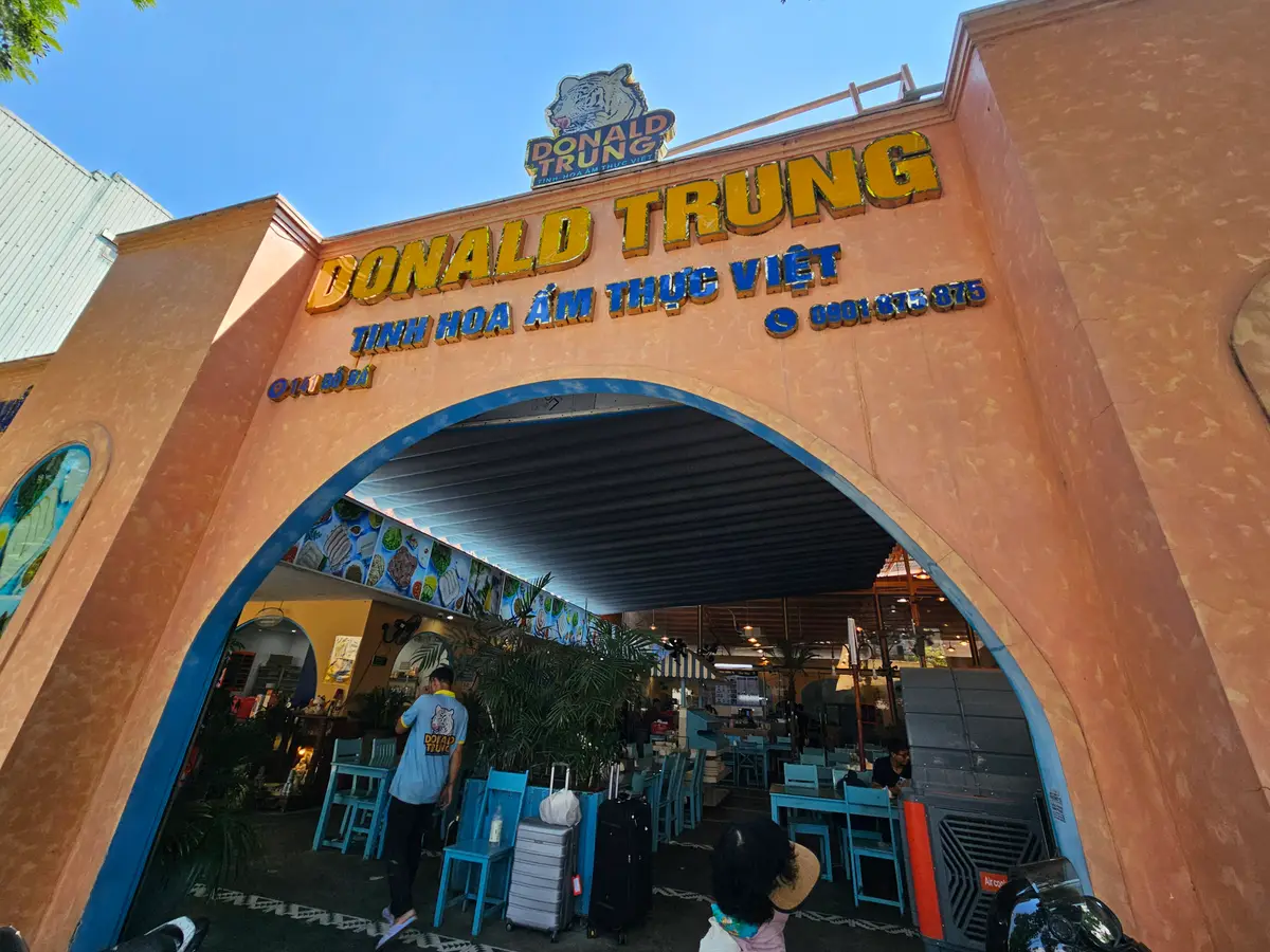 Orange arched gate of Donald Trung on Do Ba street with blue tables and chairs inside