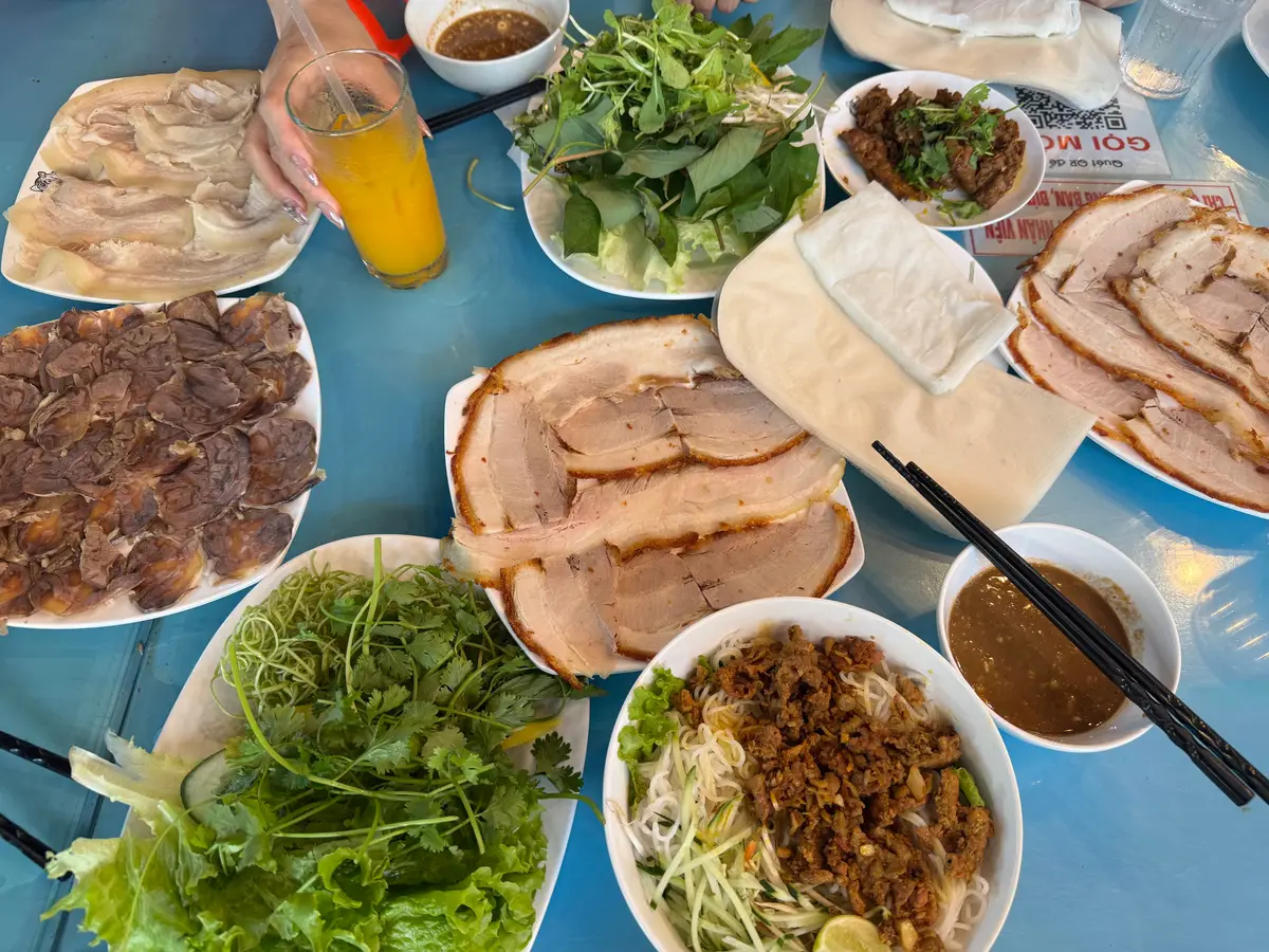 Crowded table at Donald Trung with boiled pork, herbs, rice paper, a bowl of mam and other meat plates