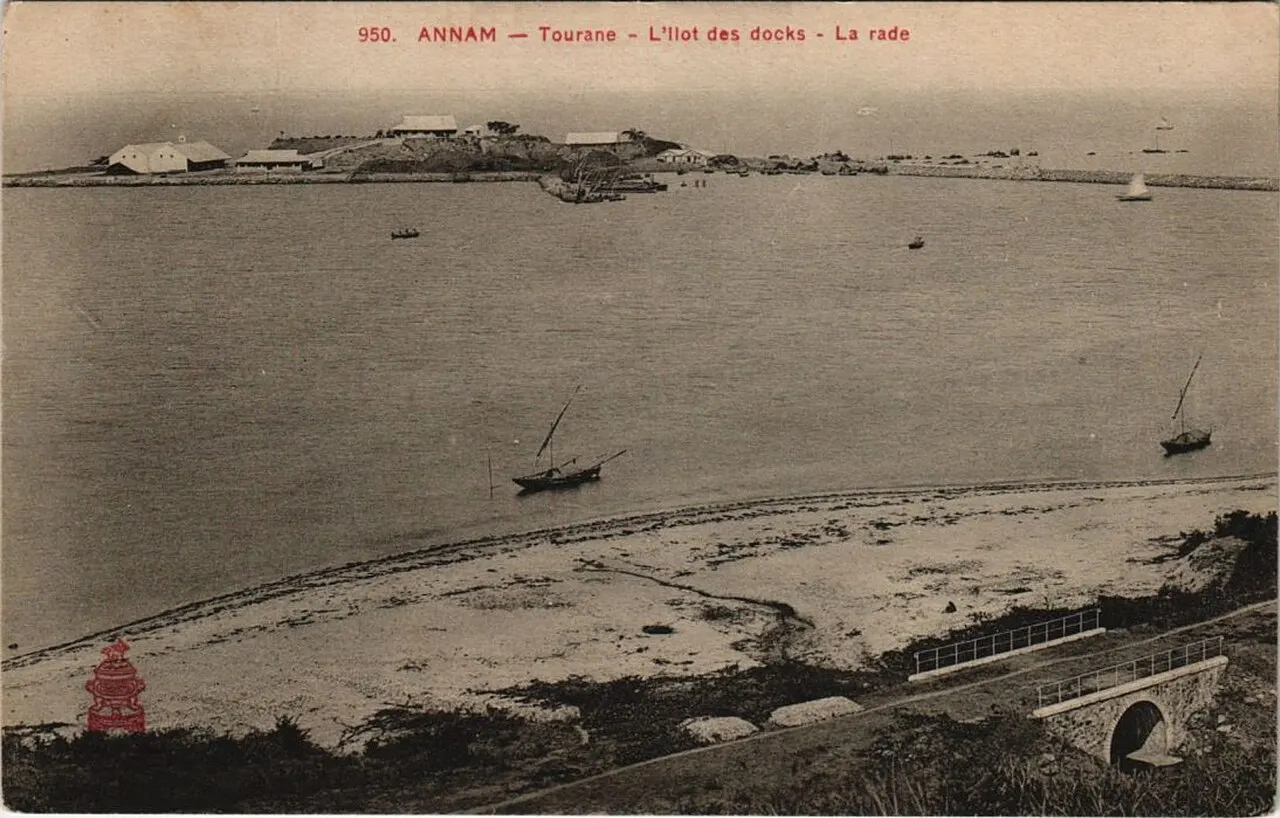 Postcard of the Tourane roadstead: low buildings on a small island, two sailing boats on calm water, a sandy beach and a stone culvert in the foreground.