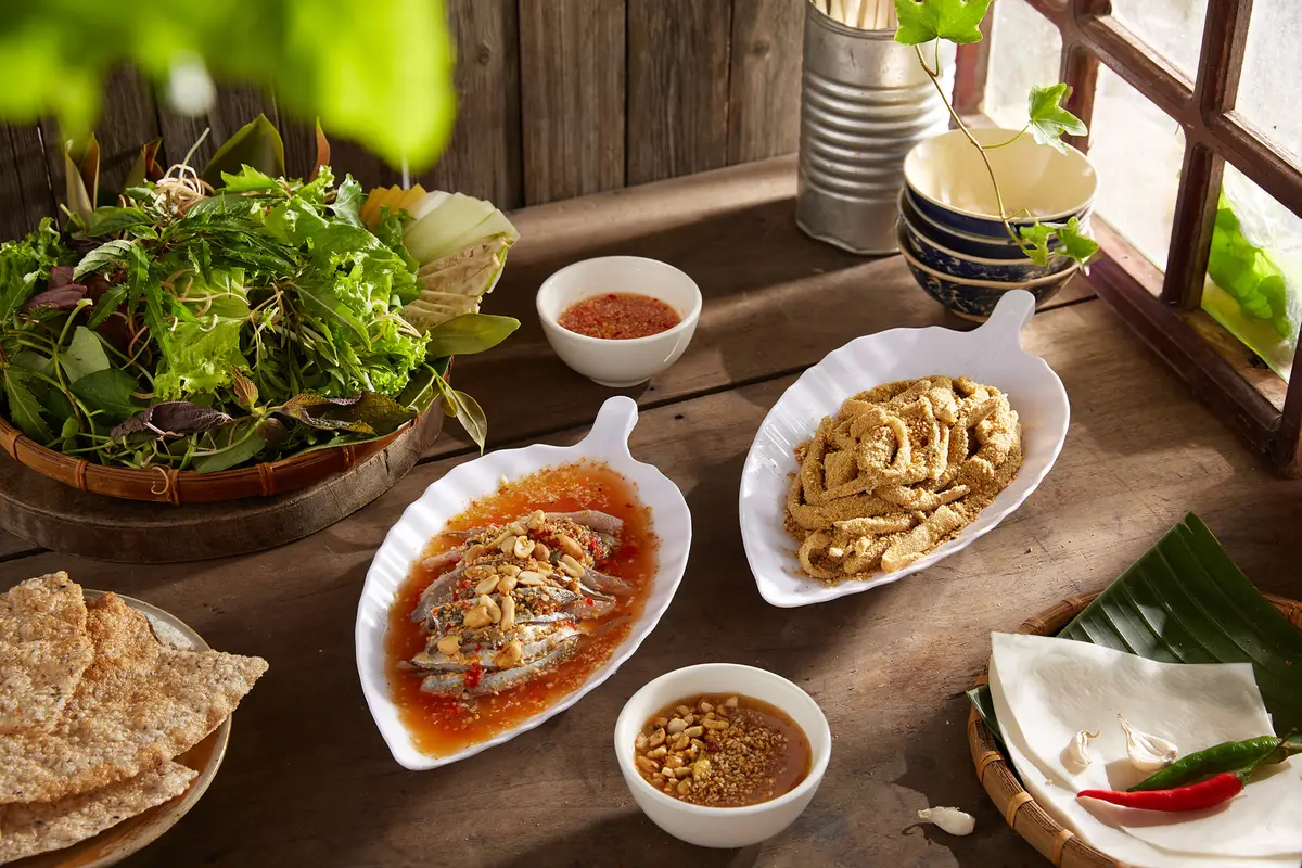 Các đĩa món ăn và đĩa rau sống trên bàn gỗ ở quán Cô Hồng.