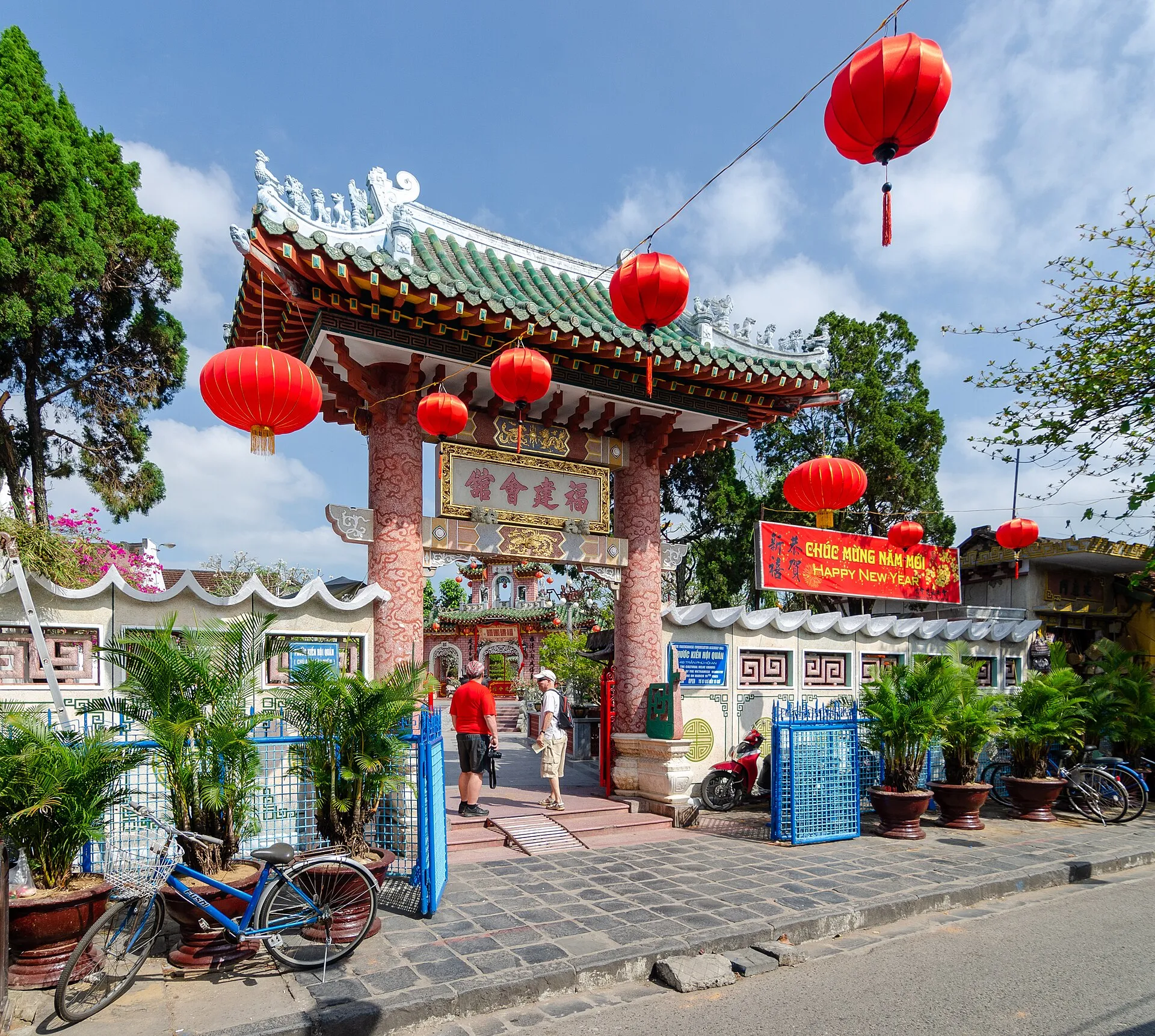 The gate of the Fujian Assembly Hall in Hoi An with a green glazed-tile roof and red lanterns hung across the street.