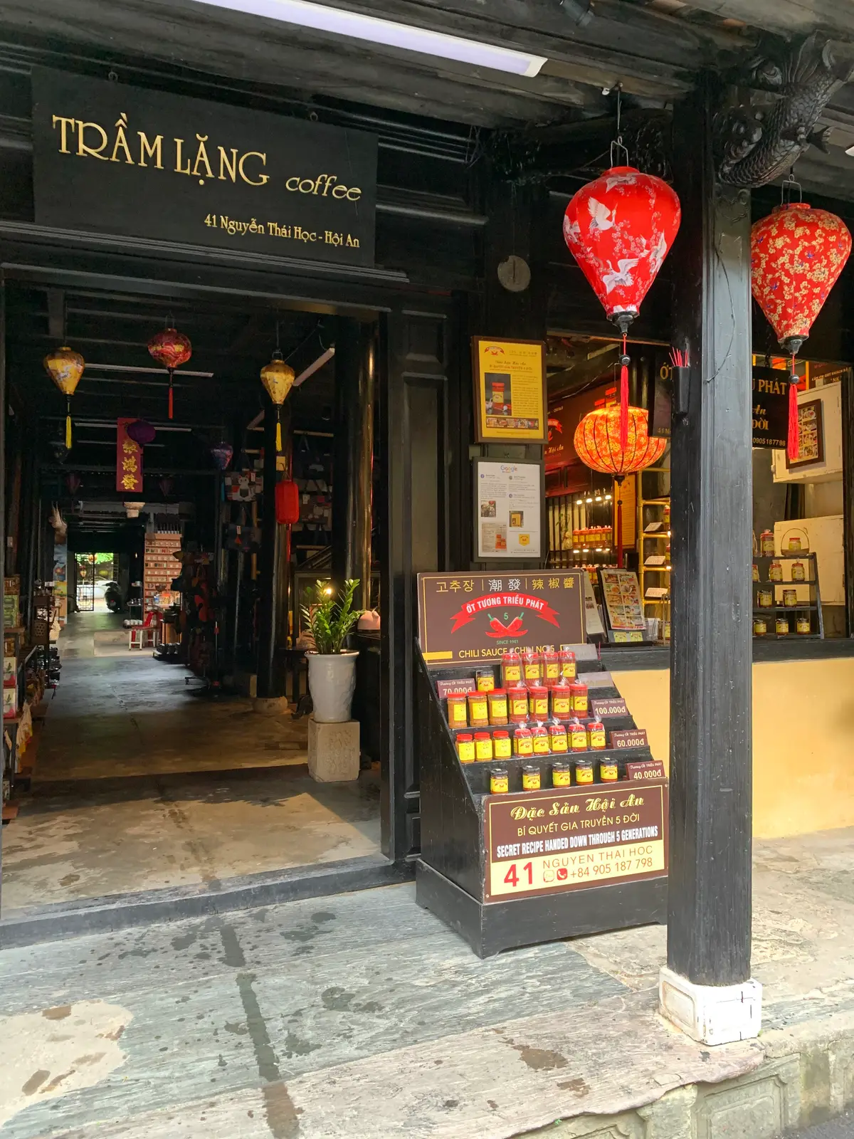 The open front of the Trieu Phat chilli sauce shop in the old house, with a display stand of jars and a lantern-hung passage behind.