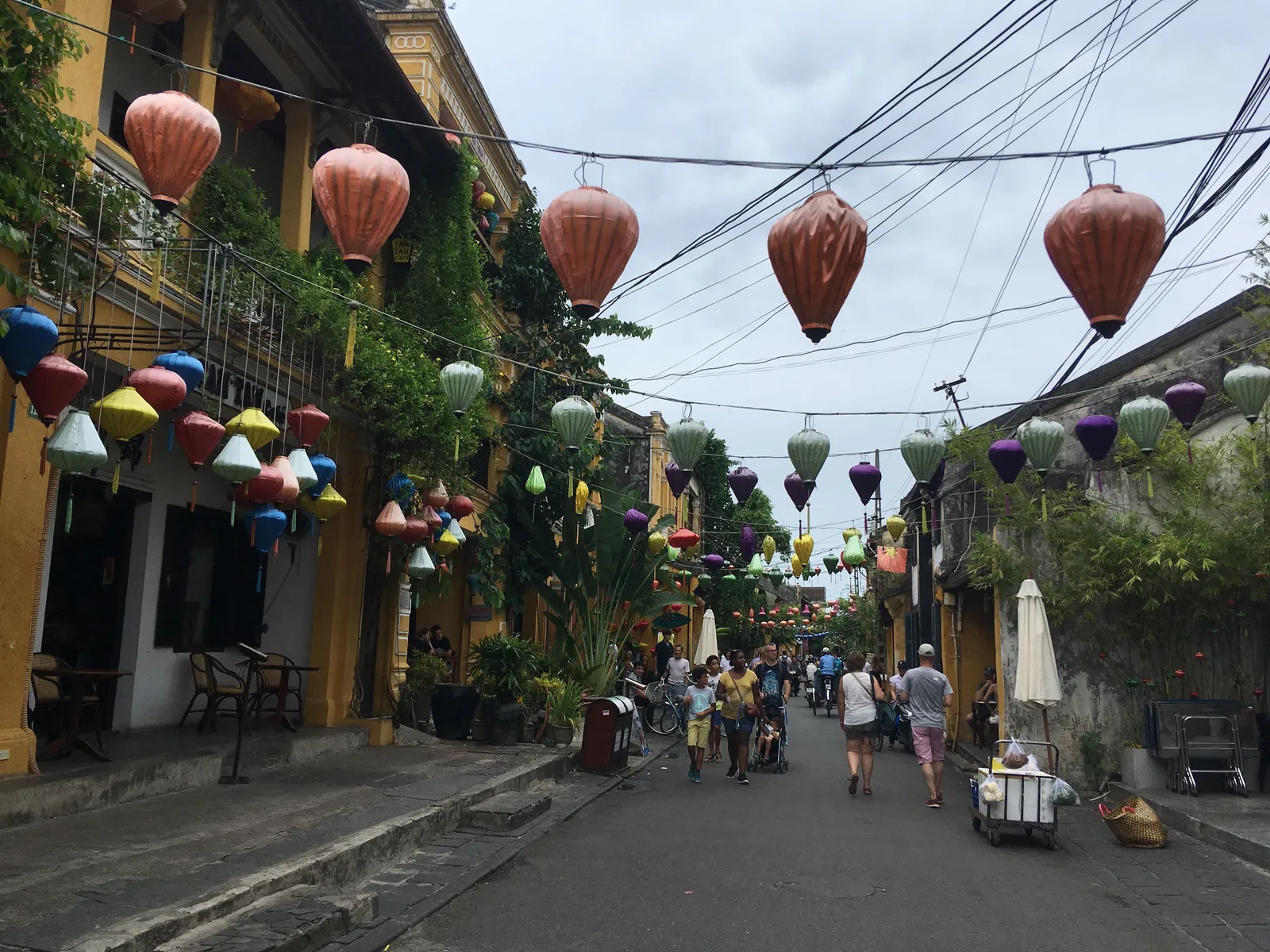 A narrow old-town street in Hoi An hung with colourful silk lanterns, with a few pedestrians walking along it.