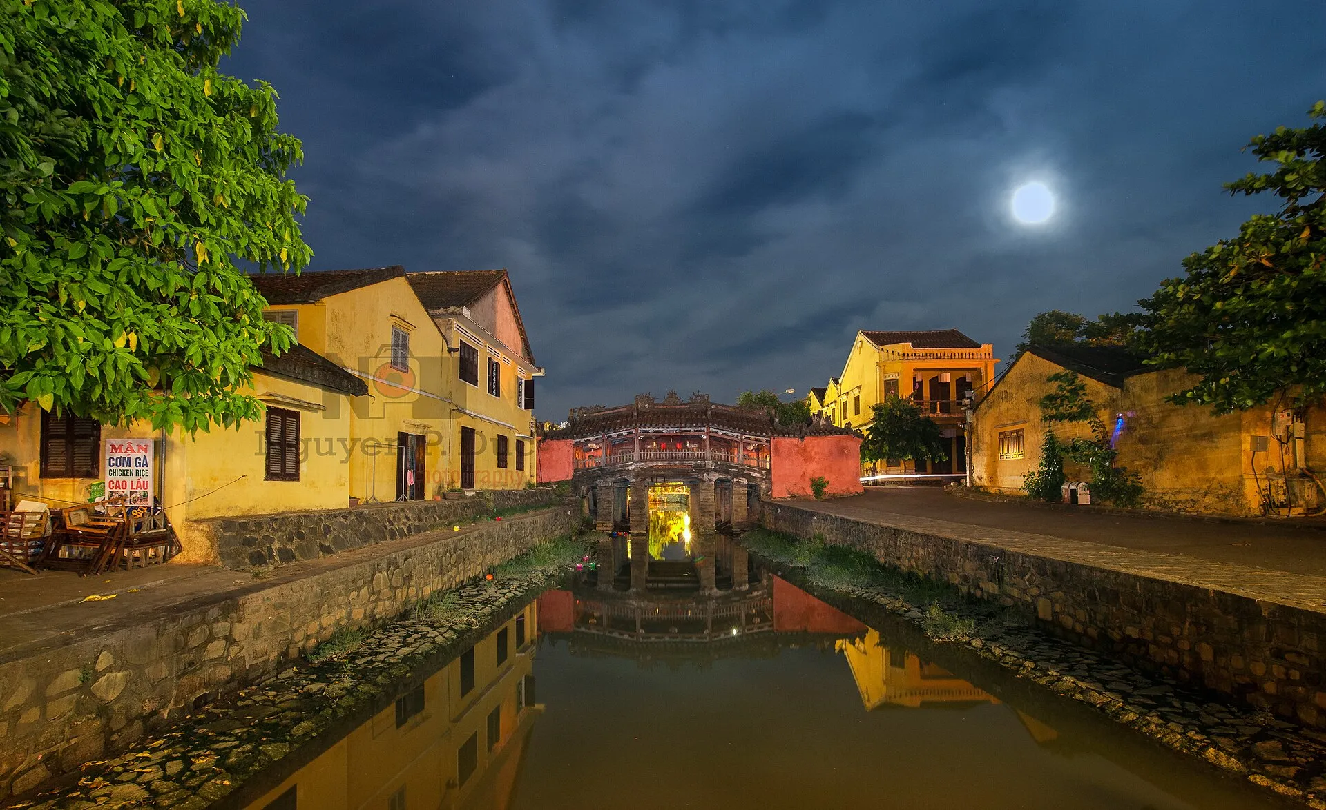 Chùa Cầu và dòng kênh dưới trăng rằm, những dãy nhà vàng sáng đèn bên bờ.