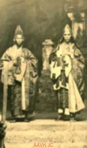 Old photograph of two monks in ceremonial dress holding prayer beads, standing in a rock cave at Ngu Hanh Son.