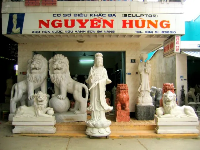 Front of a stone-carving workshop in Non Nuoc with white stone lions and a Quan Am statue displayed at the door.
