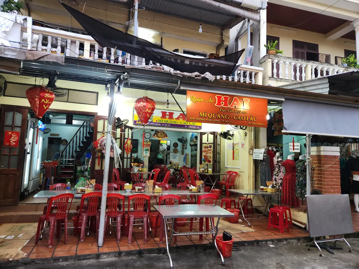 Mặt tiền quán Ông Hai trên phố, bàn ghế đỏ và đèn lồng.