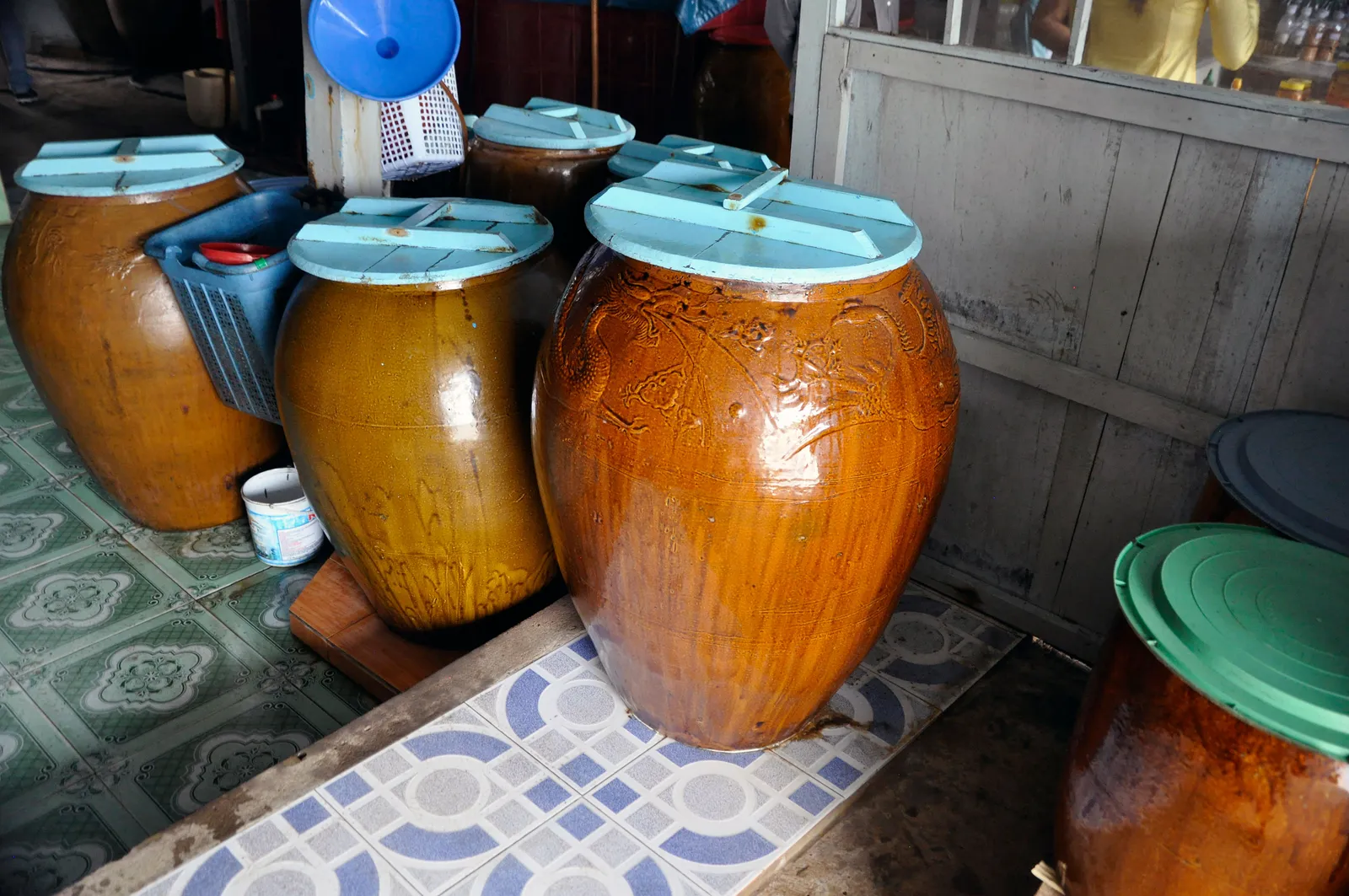 Những chum sành tráng men lớn có nắp gỗ đặt trên nền gạch trong một xưởng làm nước mắm