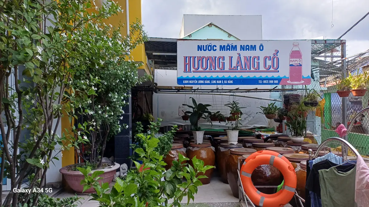 Mặt tiền xưởng Hương Làng Cổ với bảng hiệu, cây cảnh và những chum sành xếp trước cửa.