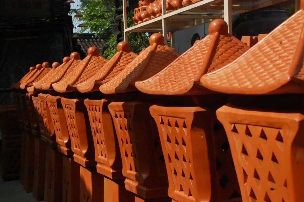 Hàng đèn lồng đất nung màu đỏ cam, khoét lỗ hoa văn, đội mái ngói nhỏ.